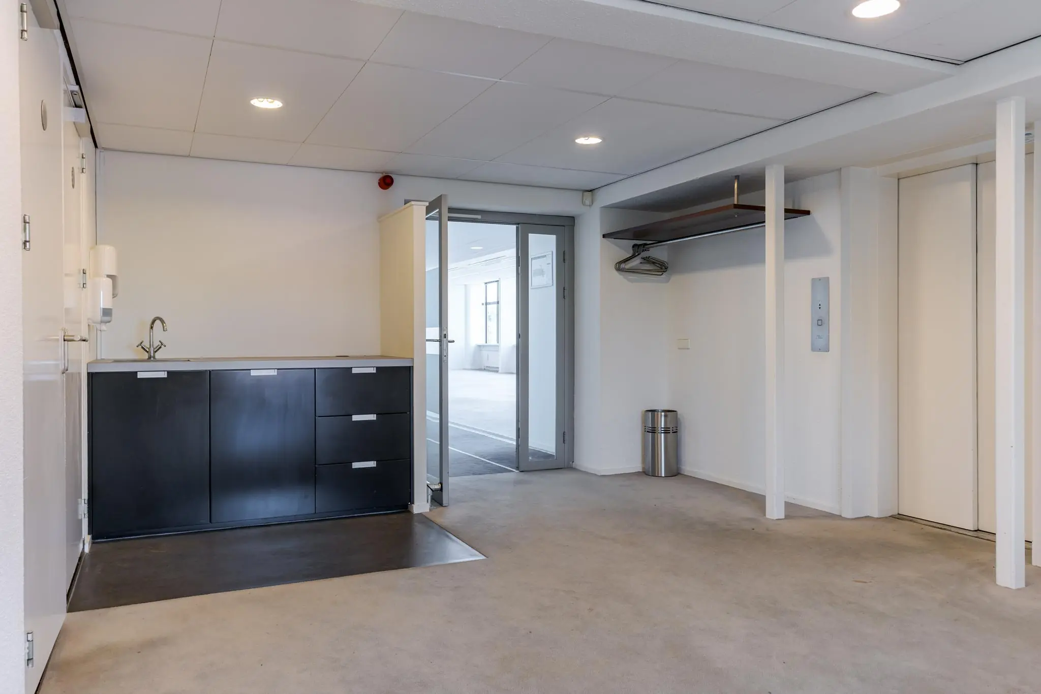 Kleine pantry-ruimte met zwarte keukenkastjes, kapstok en deur naar een licht kantoorgedeelte aan de Van Alkemadelaan.